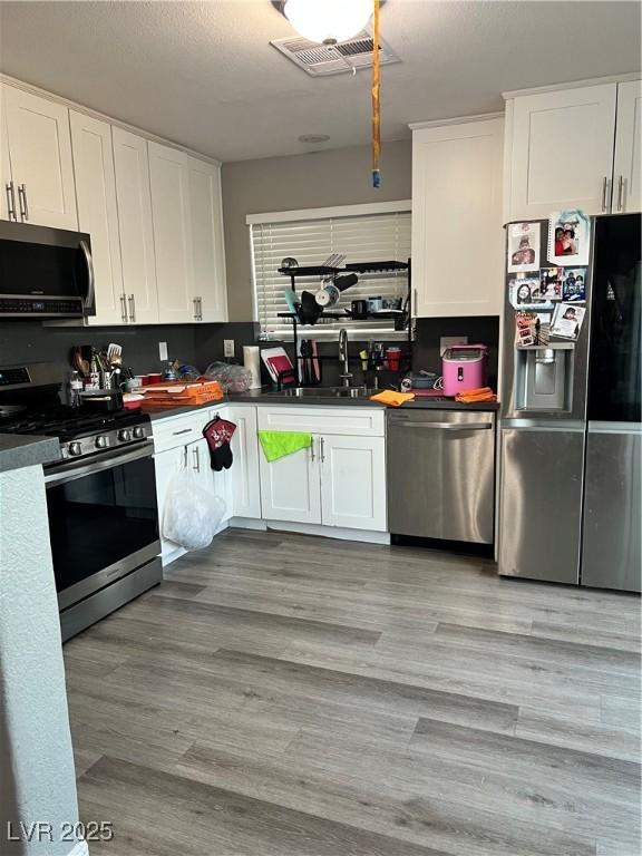 kitchen with stainless steel appliances, a sink, white cabinets, and dark countertops