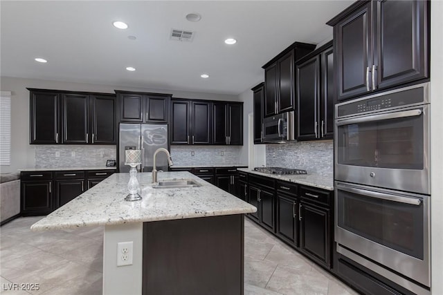 kitchen with stainless steel appliances, a sink, dark cabinetry, light stone counters, and recessed lighting