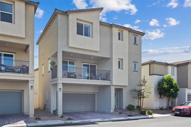 view of front of home with stucco siding, a balcony, an attached garage, and driveway