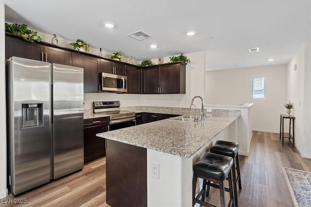 kitchen with stainless steel appliances, a sink, a peninsula, light stone counters, and light wood-style floors