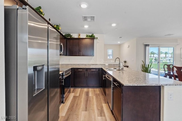 kitchen with appliances with stainless steel finishes, a peninsula, a sink, light wood finished floors, and dark brown cabinetry