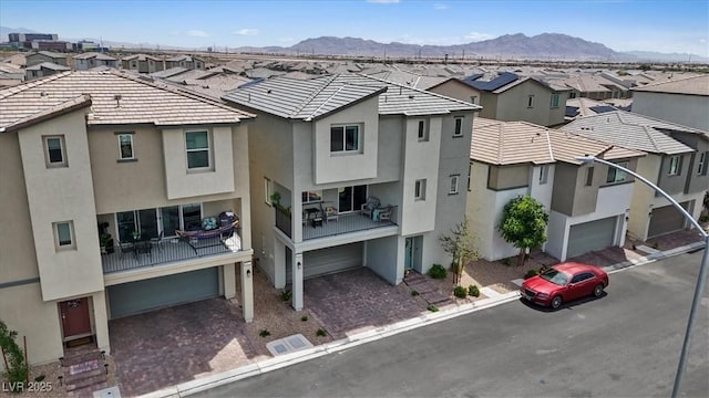 view of building exterior with a residential view, an attached garage, a mountain view, and decorative driveway