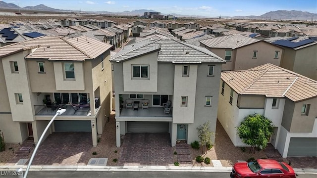 back of property featuring a residential view, an attached garage, a mountain view, stucco siding, and a balcony