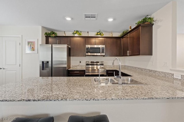 kitchen with stainless steel appliances, a sink, dark brown cabinets, a peninsula, and recessed lighting