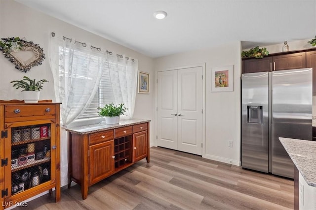 interior space with stainless steel refrigerator with ice dispenser, light stone countertops, light wood-style floors, and baseboards