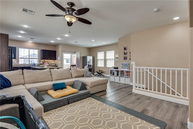 living area with wood finished floors, healthy amount of natural light, a ceiling fan, and recessed lighting