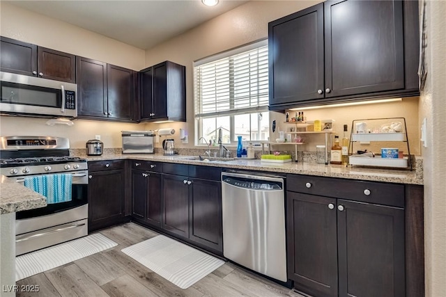 kitchen featuring stainless steel appliances, a sink, light wood-type flooring, and light stone counters