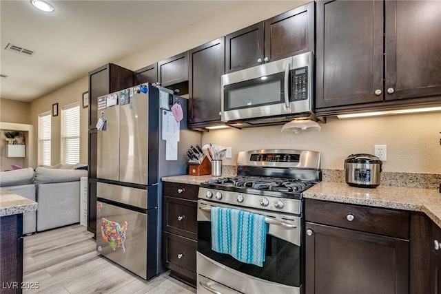 kitchen featuring stainless steel appliances, dark brown cabinets, light wood-style flooring, light stone countertops, and open floor plan
