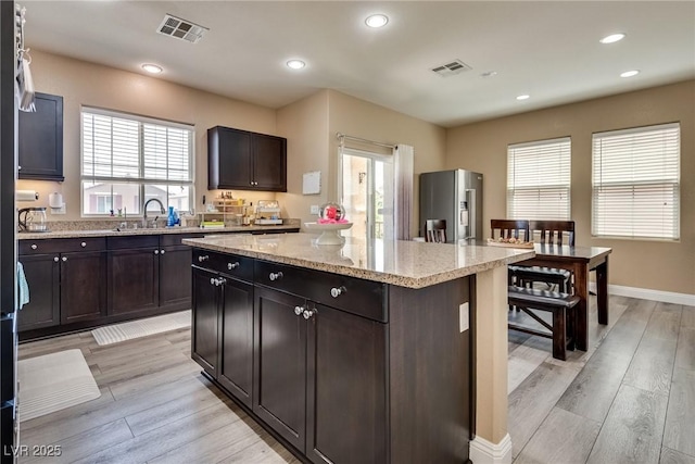 kitchen featuring stainless steel fridge with ice dispenser, a kitchen island, light stone countertops, light wood-type flooring, and recessed lighting