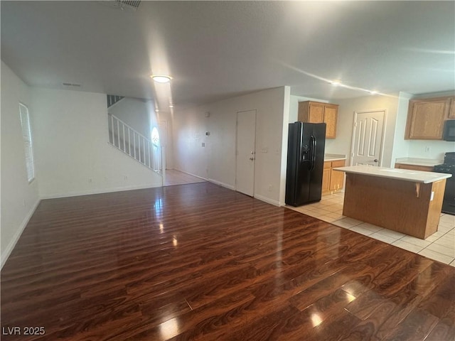 kitchen with black appliances, light wood finished floors, open floor plan, a center island, and light countertops