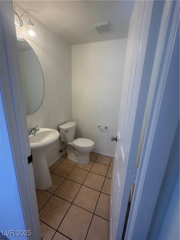 half bath with tile patterned flooring, toilet, and a sink