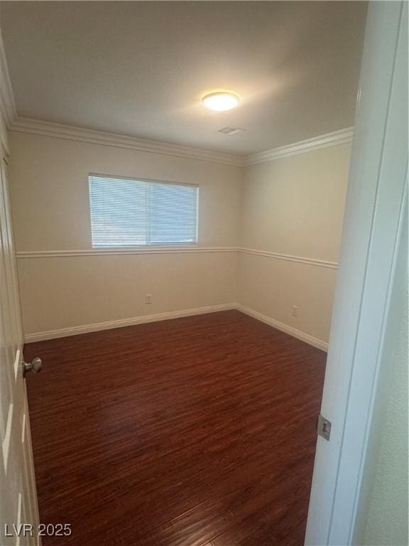 empty room with dark wood finished floors, crown molding, and baseboards