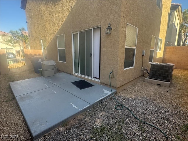 rear view of house with stucco siding, central air condition unit, fence, and a patio