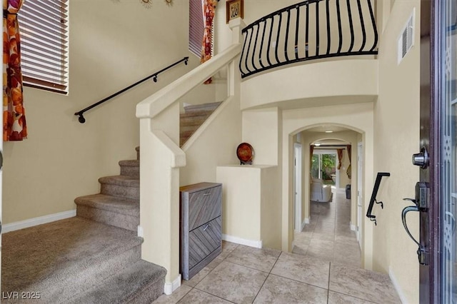foyer entrance featuring arched walkways, baseboards, stairway, tile patterned floors, and a towering ceiling