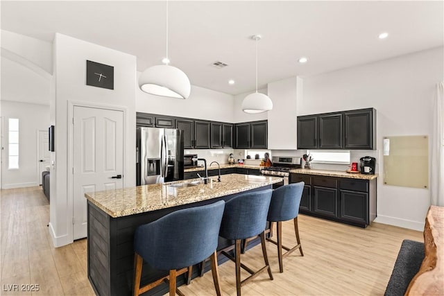 8317 Fritzen Ave, Las Vegas, NV 89131 - kitchen with stainless steel appliances, a sink, dark cabinetry, light wood-style flooring, and light stone countertops