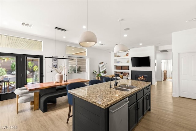 8317 Fritzen Ave, Las Vegas, NV 89131 - kitchen featuring dishwasher, a sink, a kitchen island with sink, dark cabinetry, and a glass covered fireplace