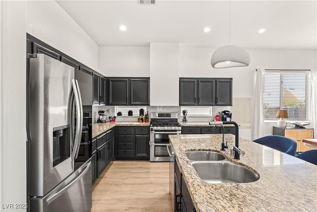8317 Fritzen Ave, Las Vegas, NV 89131 - kitchen with stainless steel appliances, a sink, dark cabinets, light stone counters, and light wood-style floors