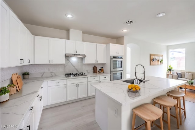 3065 Blue Monaco St, Las Vegas, NV 89117 - kitchen with appliances with stainless steel finishes, light wood finished floors, under cabinet range hood, arched walkways, and a breakfast bar