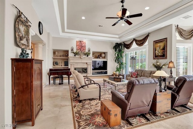 living room with plenty of natural light, a raised ceiling, crown molding, a ceiling fan, and a glass covered fireplace