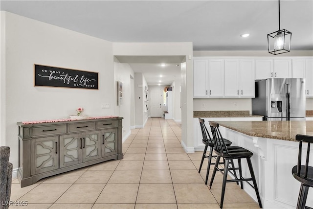 7545 Fontera Ct, Las Vegas, NV 89139 - kitchen with stainless steel fridge, a breakfast bar, light tile patterned floors, dark stone counters, and white cabinets