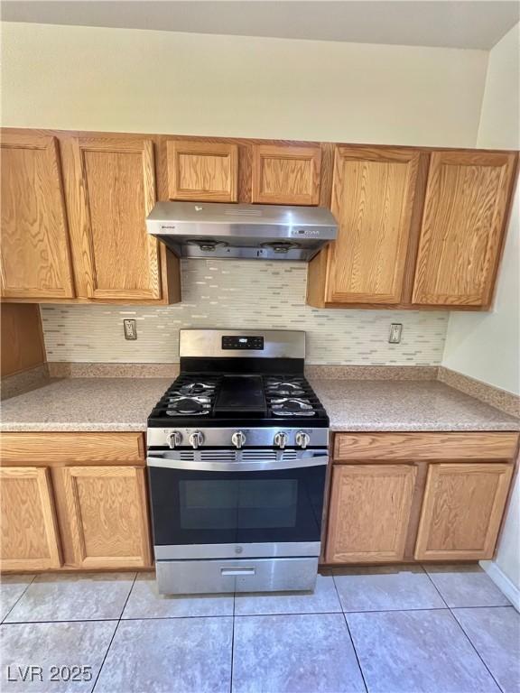 6545 Netherseal Ave, Las Vegas, NV 89139 - kitchen with under cabinet range hood, stainless steel gas stove, light countertops, decorative backsplash, and light tile patterned floors