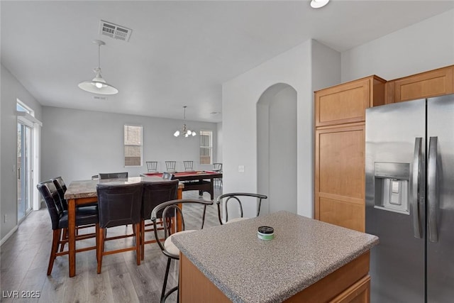 kitchen featuring stainless steel fridge with ice dispenser, light wood finished floors, arched walkways, pendant lighting, and a center island