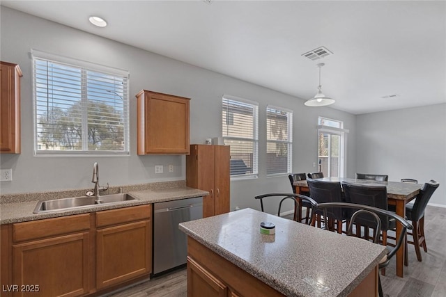 kitchen with stainless steel dishwasher, a sink, light wood-type flooring, brown cabinets, and pendant lighting