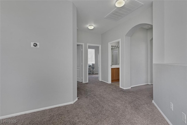 corridor featuring carpet flooring, arched walkways, and baseboards