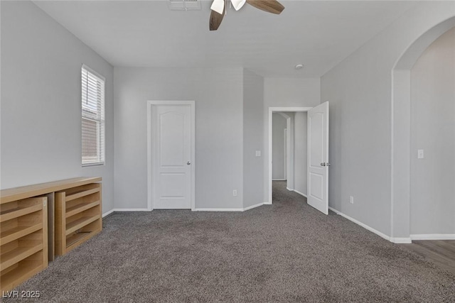 carpeted empty room with arched walkways, a ceiling fan, and baseboards
