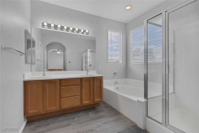 bathroom featuring a stall shower, a bath, wood finished floors, double vanity, and recessed lighting
