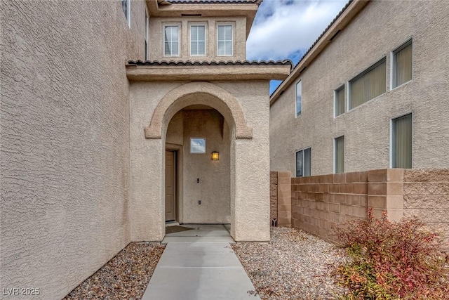 view of exterior entry with a tile roof, stucco siding, and fence