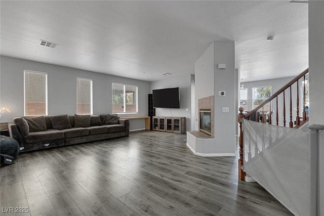 living area with a tile fireplace, dark wood finished floors, baseboards, and stairway