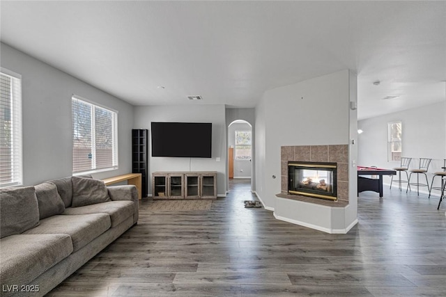 living area with wood finished floors, a tile fireplace, and arched walkways