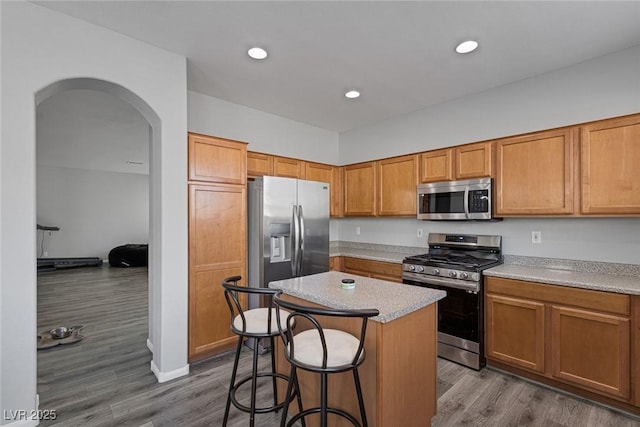 kitchen with stainless steel appliances, arched walkways, a center island, a kitchen bar, and light countertops