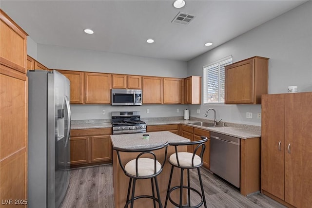 kitchen with appliances with stainless steel finishes, a sink, a kitchen island, light wood-style floors, and recessed lighting