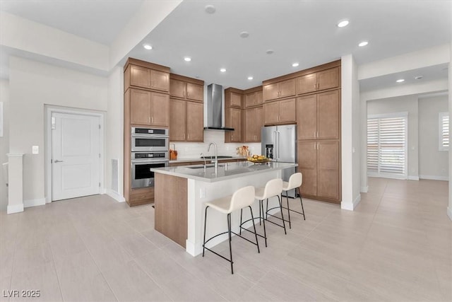 kitchen featuring wall chimney range hood, appliances with stainless steel finishes, recessed lighting, baseboards, and a kitchen bar
