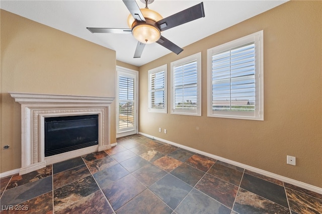8547 Benidorm Ave, Las Vegas, NV 89178 - unfurnished living room with baseboards, stone tile flooring, a glass covered fireplace, and a ceiling fan