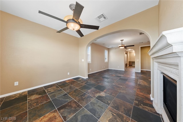 8547 Benidorm Ave, Las Vegas, NV 89178 - unfurnished living room featuring a ceiling fan, arched walkways, stone tile flooring, baseboards, and a fireplace