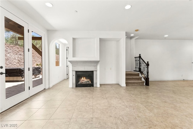 1252 Casa Palermo Cir, Henderson, NV 89011 - unfurnished living room featuring stairway, recessed lighting, light tile patterned flooring, a warm lit fireplace, and arched walkways