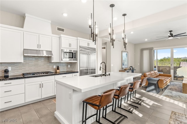 kitchen featuring built in appliances, a sink, under cabinet range hood, light tile patterned floors, and recessed lighting