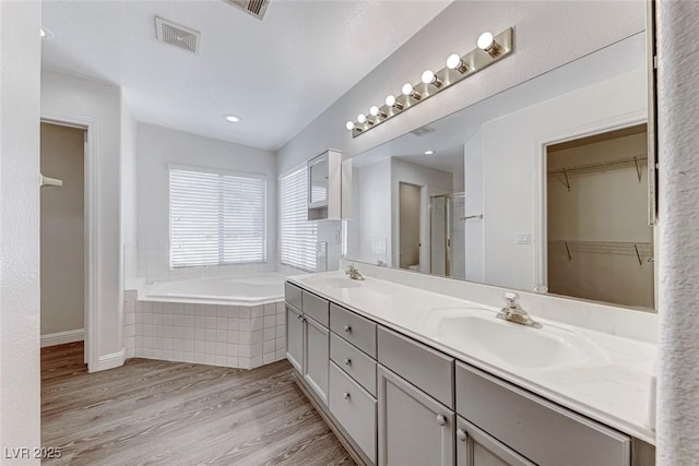 11028 Meadow Leaf Ave, Las Vegas, NV 89144 - full bathroom featuring wood finished floors, a bath, double vanity, a stall shower, and a walk in closet