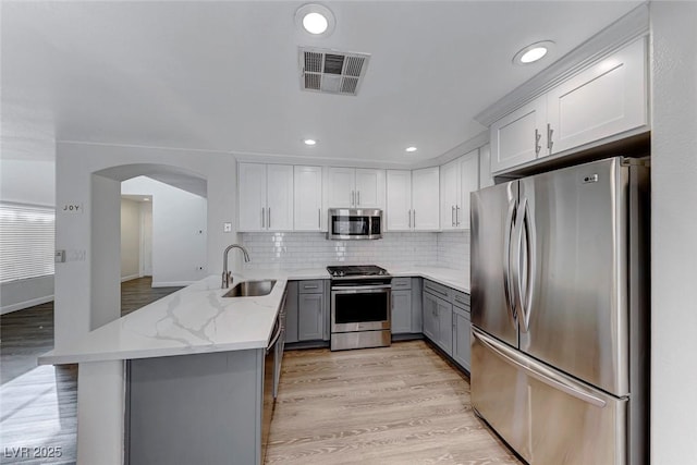 11028 Meadow Leaf Ave, Las Vegas, NV 89144 - kitchen with appliances with stainless steel finishes, a sink, gray cabinets, a peninsula, and arched walkways