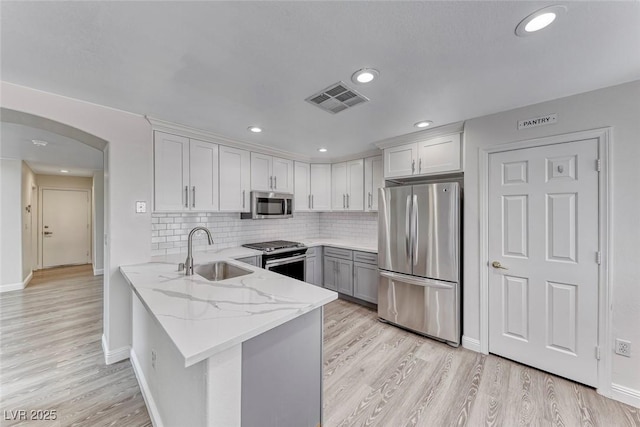 11028 Meadow Leaf Ave, Las Vegas, NV 89144 - kitchen featuring appliances with stainless steel finishes, a sink, a peninsula, arched walkways, and light stone countertops