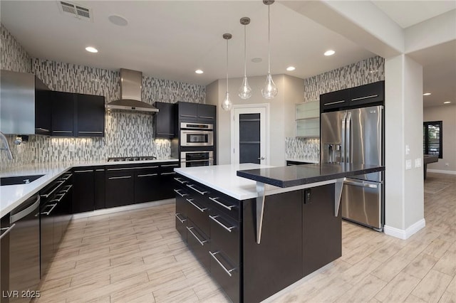 2900 Valvent Ct, Henderson, NV 89044 - kitchen with wall chimney range hood, stainless steel appliances, light wood-style flooring, dark cabinetry, and a center island