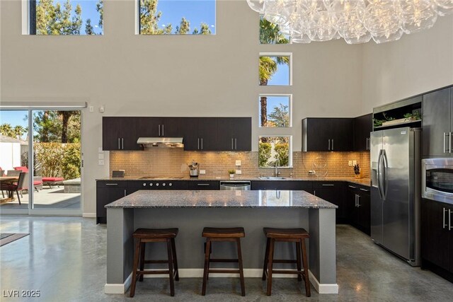 2672 Mystere Ct, Las Vegas, NV 89117 - kitchen with stainless steel appliances, a towering ceiling, under cabinet range hood, a chandelier, and a breakfast bar area