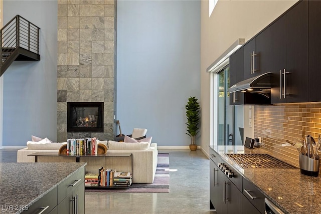 2672 Mystere Ct, Las Vegas, NV 89117 - kitchen featuring stainless steel gas cooktop, a fireplace, decorative backsplash, dark stone counters, and a high ceiling