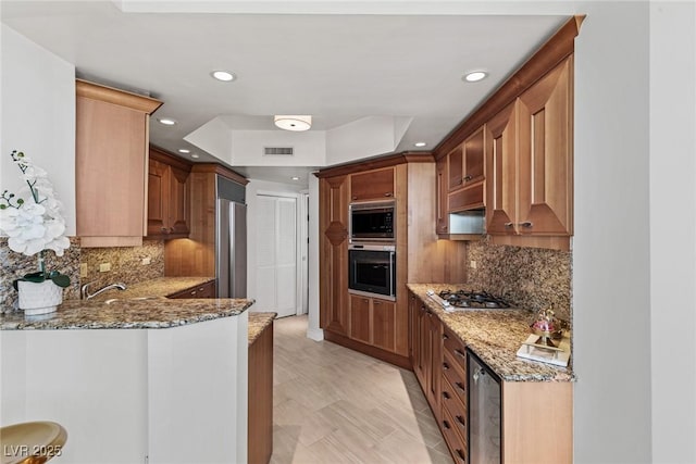 kitchen featuring appliances with stainless steel finishes, light stone counters, a tray ceiling, backsplash, and recessed lighting