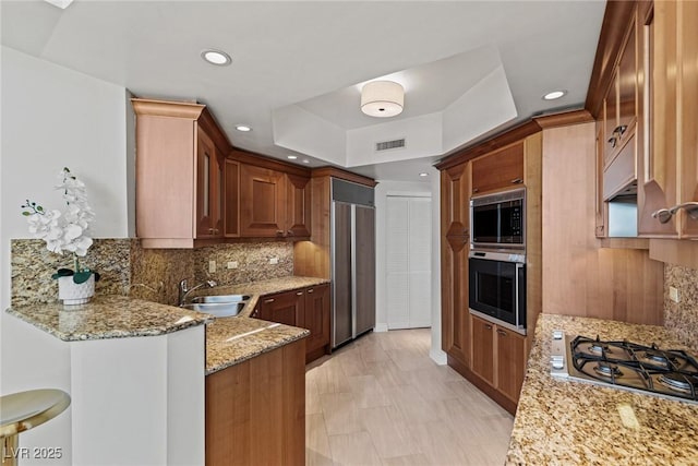 kitchen featuring built in appliances, a sink, light stone counters, a peninsula, and tasteful backsplash
