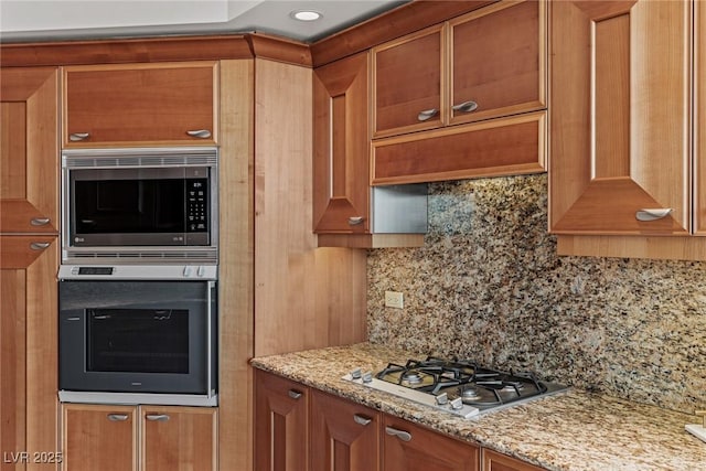 2777 Paradise Rd Unit 1105, Las Vegas, NV 89109 - kitchen featuring appliances with stainless steel finishes, backsplash, light stone counters, and brown cabinets