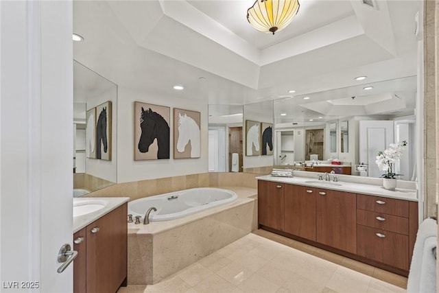bathroom with a raised ceiling, two vanities, a bath, and tile patterned flooring